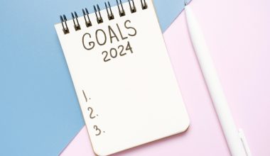 A notepad that says "Goals 2024" with three lines numbered 1, 2, and 3 with a white pen next to it over a background that is half blue and half pink.