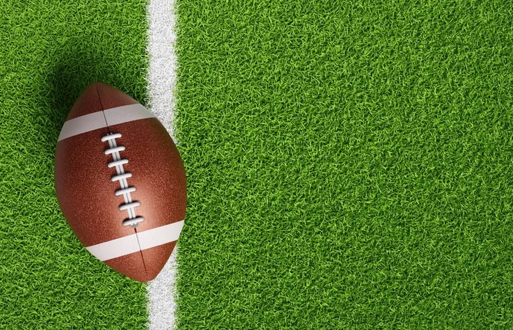 An American football on green turf next to a white line.