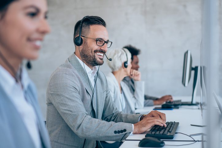 A cheerful man in a call center, equipped with headphones, providing assistance to a client over the phone.