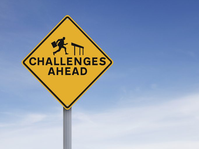 A yellow road sign reads "CHALLENGES AHEAD" with a figure running towards a hurdle.