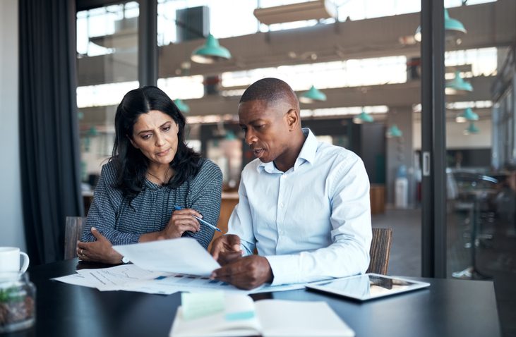 Two people reviewing documents at a table in a well-lit office.