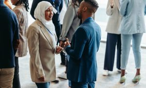 People networking at an event, including a woman in a hijab and a man in a suit talking closely.