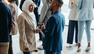 People networking at an event, including a woman in a hijab and a man in a suit talking closely.