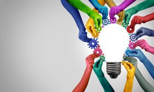 Hands of different colors assemble gears around a light bulb outline, with a gradient background from gray to white.