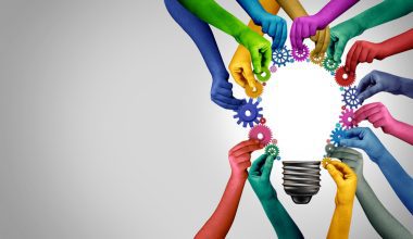 Hands of different colors assemble gears around a light bulb outline, with a gradient background from gray to white.