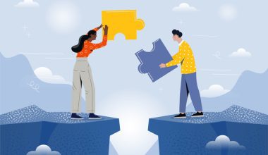 Two people on opposite sides of a gap holding large puzzle pieces, symbolizing collaboration and bridging roles, with a sky and mountain backdrop.