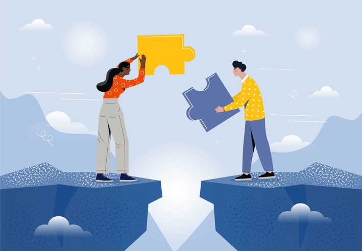 Two people on opposite sides of a gap holding large puzzle pieces, symbolizing collaboration and bridging roles, with a sky and mountain backdrop.