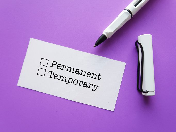 A white card with two checkboxes labeled "Permanent" and "Temporary" is placed on a purple surface. Next to the card, there is a white pen with a black tip and a white cap attached to it by a black string.