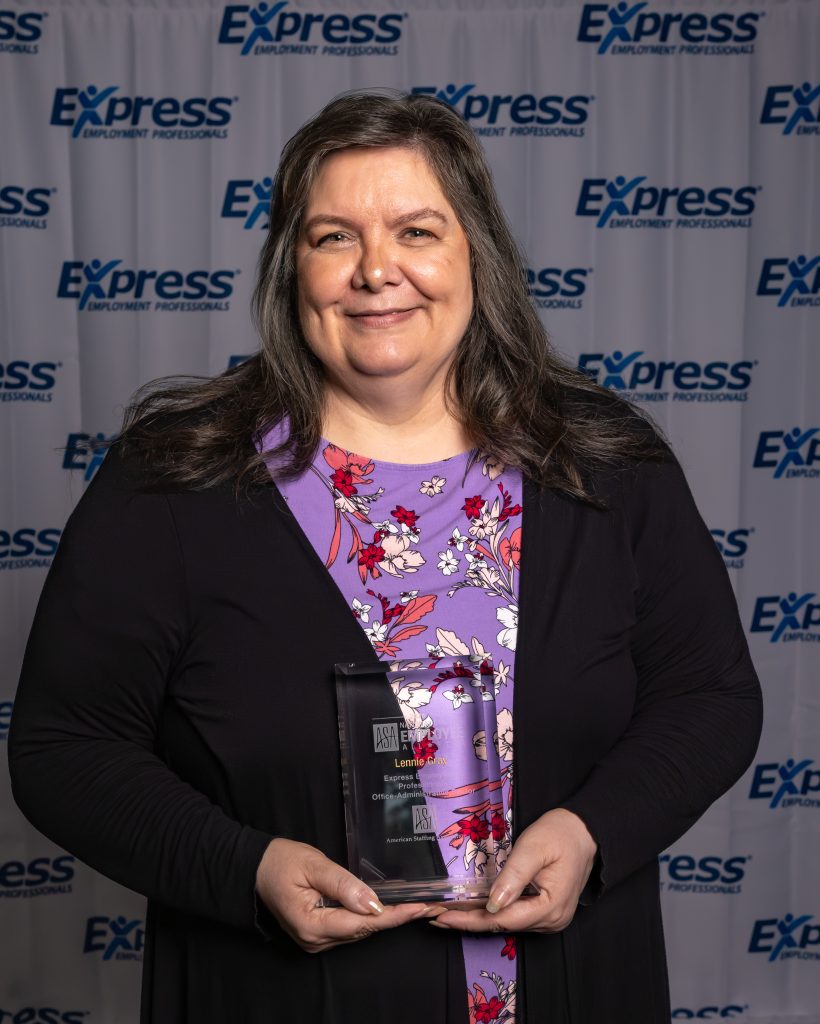 Lennie Gray holding a National Staffing All-Star award in front of an Express Employment Professionals backdrop, wearing a purple floral top and black cardigan.