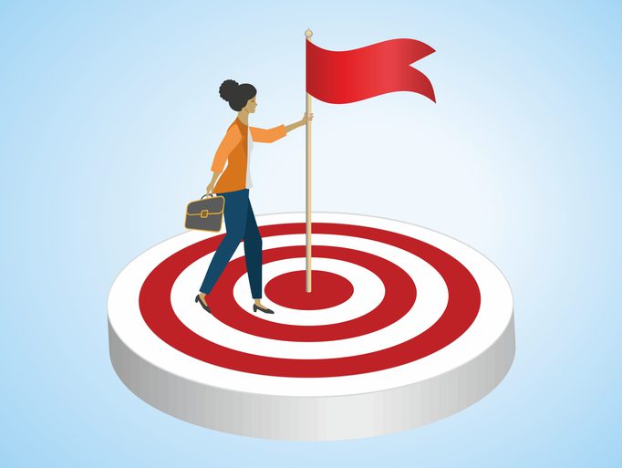 Business professional standing on a red-and-white target holding a flag, symbolizing achieving leadership goals and success.