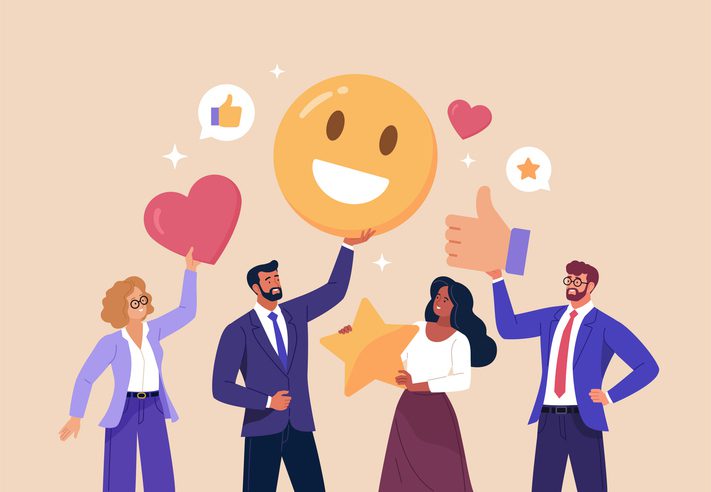 Four business professionals standing together holding large icons representing positive feedback, including a smiling emoji, a heart, a star, and a thumbs-up symbol, with speech bubbles showing likes and ratings.