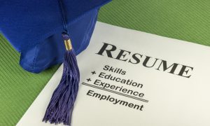 A graduation cap resting on a resume that highlights skills, education, and experience.