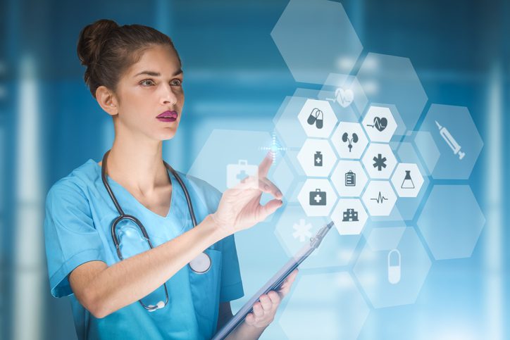A healthcare professional in blue scrubs uses a tablet and gestures toward a transparent digital interface displaying medical icons and health data in a modern clinical setting.