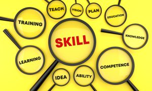 Illustration of multiple magnifying glasses on a bright yellow background, with the largest lens highlighting the word “SKILL.” Surrounding lenses contain the words “TRAINING,” “LEARNING,” “TEACH,” “VISION,” “PLAN,” “EDUCATION,” “KNOWLEDGE,” “COMPETENCE,” “ABILITY,” and “IDEA,” emphasizing workforce development, education, and professional skills.